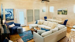 A spacious living room with a high ceiling, a ceiling fan, a dining area with a table and chairs, and a large window. - Private Hot Tub home + separate 1st floor studio (Port Aransas)