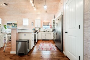 A compact kitchen with white cabinetry, a stainless steel refrigerator, and a wooden floor.