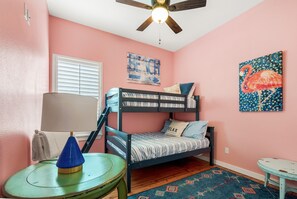 A bedroom with pink walls, a bunk bed, a ceiling fan, a lamp, a small table, and a rug.
