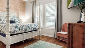 A bedroom with a four-poster bed, a wooden headboard, a wicker chair, a wooden cabinet, and a television on the wall. - Private Hot Tub home + separate 1st floor studio (Port Aransas)