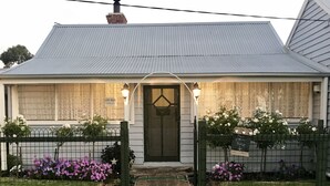 Uma casa com telhado de metal corrugado, porta frontal e uma placa com a mensagem 'Free, por favor, pegue'.