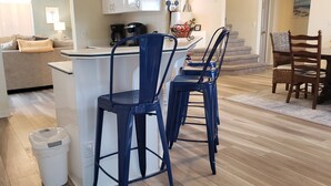 Una cocina con mostrador blanco, taburetes de bar azules y una cafetera.