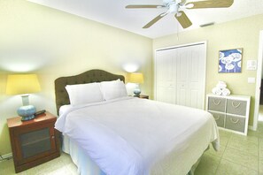 Une chambre à coucher comprenant un lit, des tables de chevet, un ventilateur de plafond, une armoire et une lampe fixée au mur.