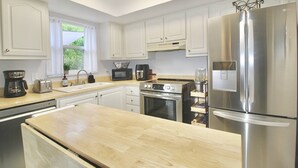A modern kitchen with white cabinets, stainless steel appliances, and a wooden countertop.