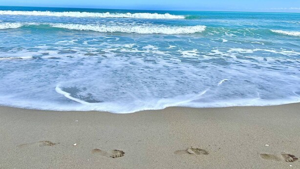 A beach with waves and footprints in the sand.