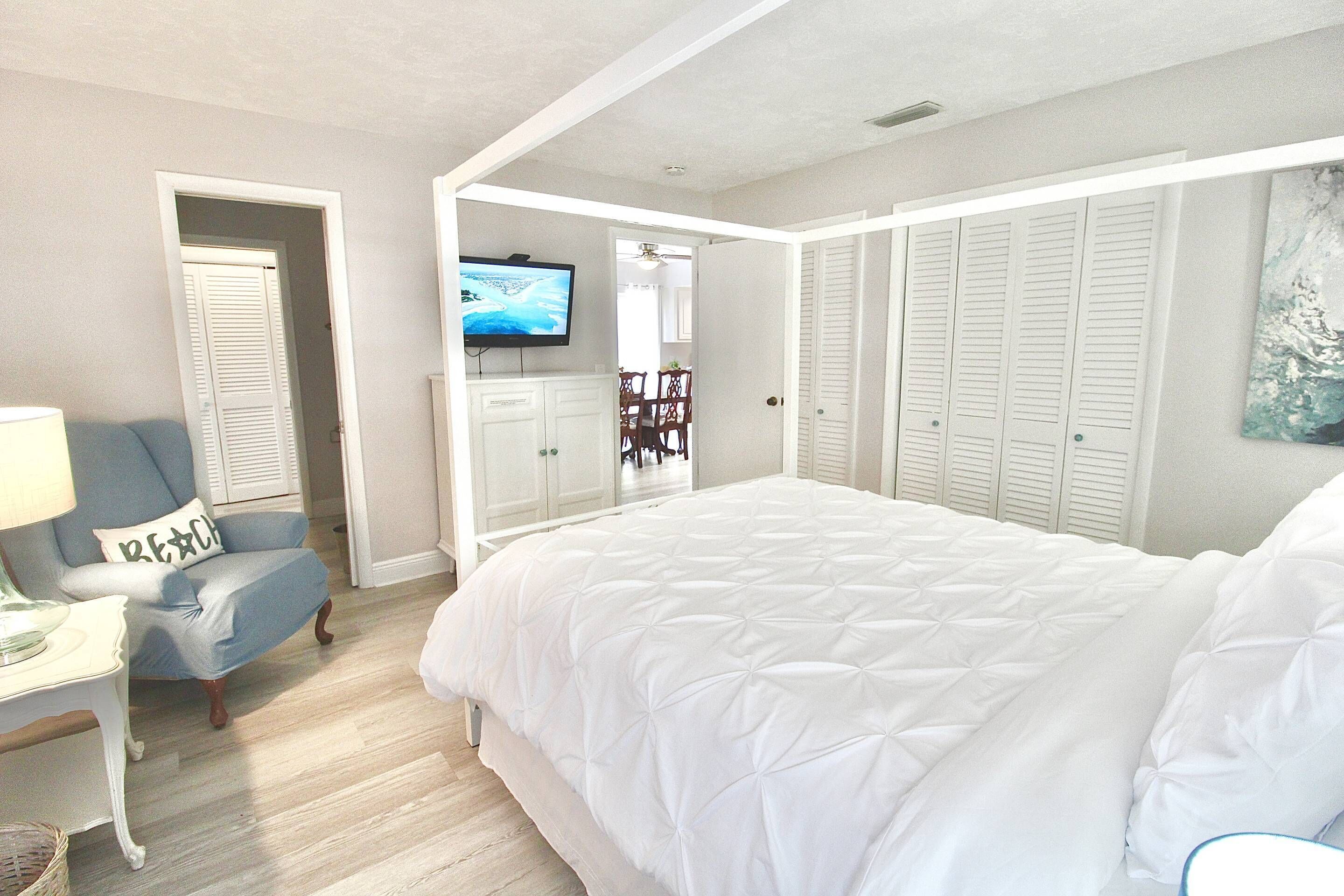 A bedroom with a large bed, a TV, a chair, and a wardrobe.