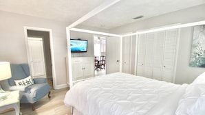 A bedroom with a large bed, a TV, a chair, and a wardrobe.