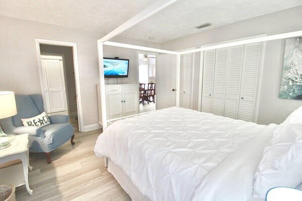A bedroom with a large bed, a TV, a chair, and a wardrobe.