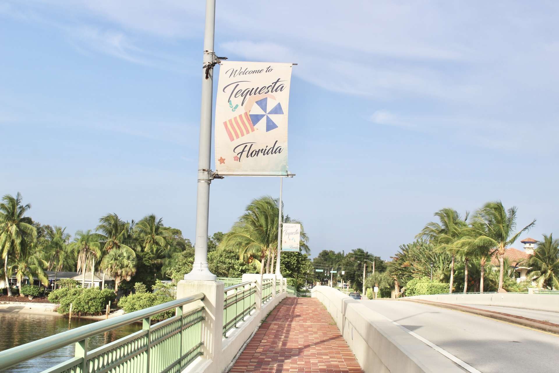 A bridge with a banner reading "Welcome to Tequesta Florida" and a view of palm trees and a body of water.