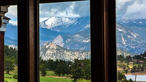 Un paysage de montagne vu à travers une fenêtre, avec en toile de fond des sommets enneigés et des vallées boisées.
