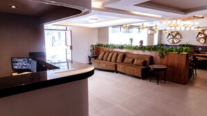 A reception area with a curved counter, a sofa, and a wooden planter with plants. - Hotel Melanie Tepic (Tepic)
