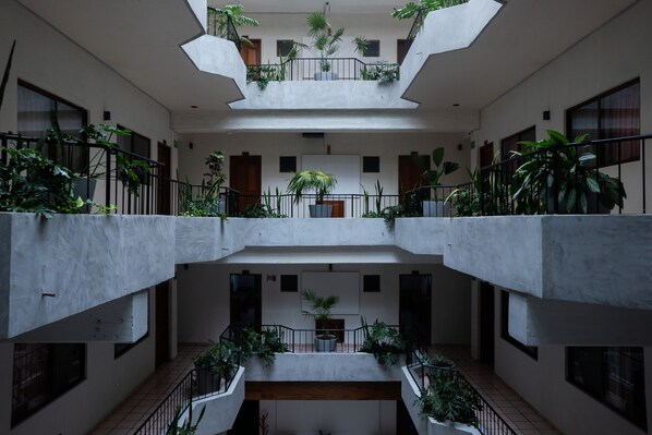 A multi-level atrium with concrete floors and railings, featuring potted plants and a central staircase.