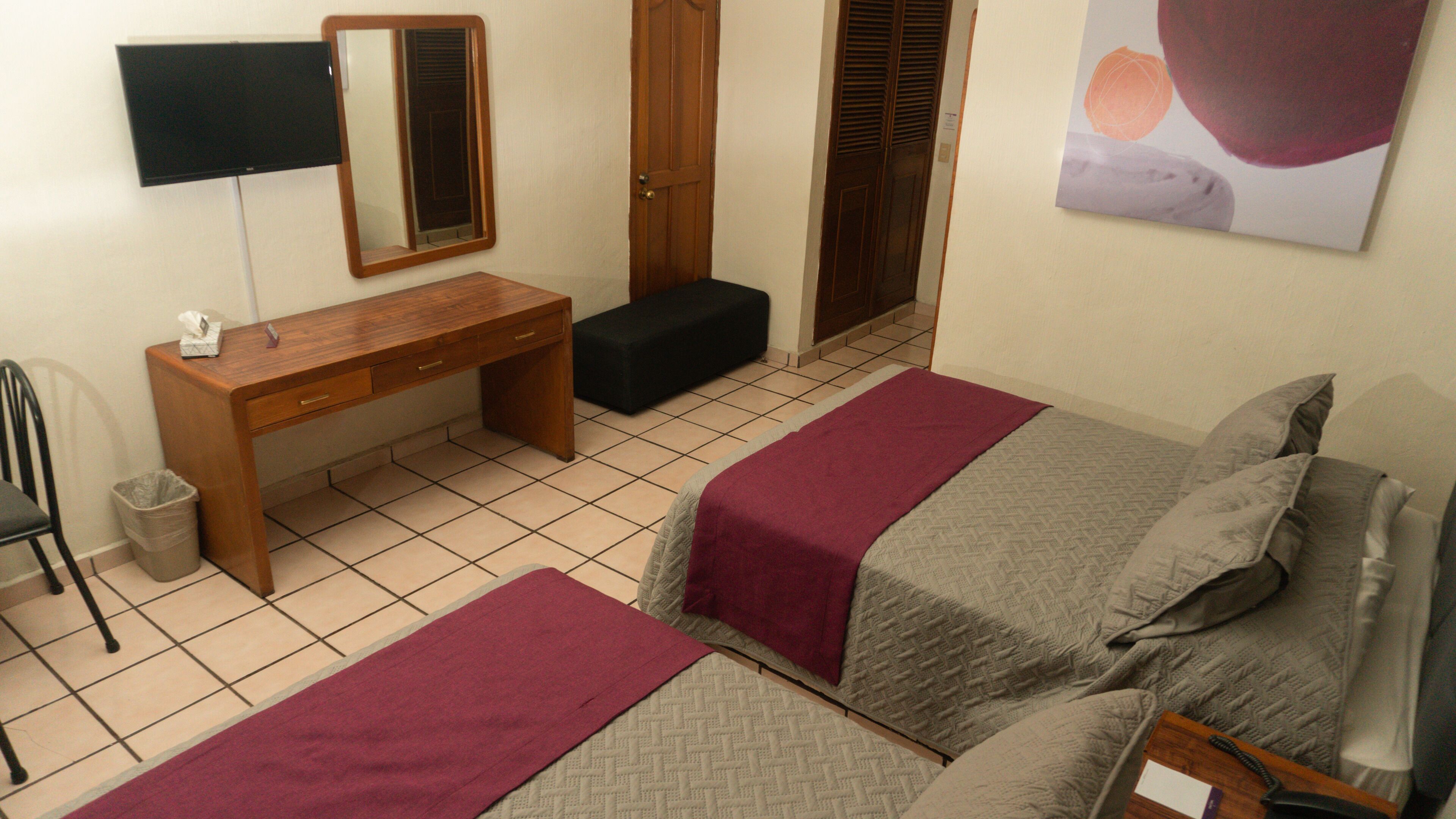 Een slaapkamer met twee bedden, een houten bureau, een stoel, een prullenbak en een spiegel.