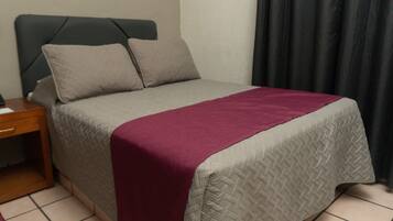 A neatly made bed with a grey and white quilt, a red blanket, and two pillows.