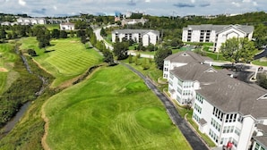 An aerial view of a golf course with a residential area nearby, including multi-story buildings and a road. - Little House on the Fairway- Luxury Golf Condo (Branson)