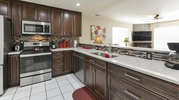 A modern kitchen with dark wood cabinets, stainless steel appliances, a tiled backsplash, and a red rug. - Little House on the Fairway- Luxury Golf Condo (Branson)