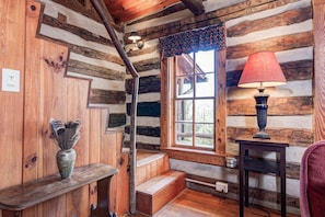 L’intérieur d’un chalet rustique, avec un banc en bois, une lampe et une fenêtre donnant sur le paysage extérieur.