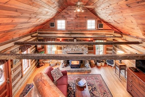 L’intérieur d’une cabane en rondins, avec une cheminée en pierre, des poutres en bois, un canapé rouge et un téléviseur.