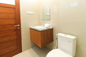 A bathroom with a wooden door, a white sink, a mirror, and a toilet. - Manu Guest House 2 (Tibubeneng)