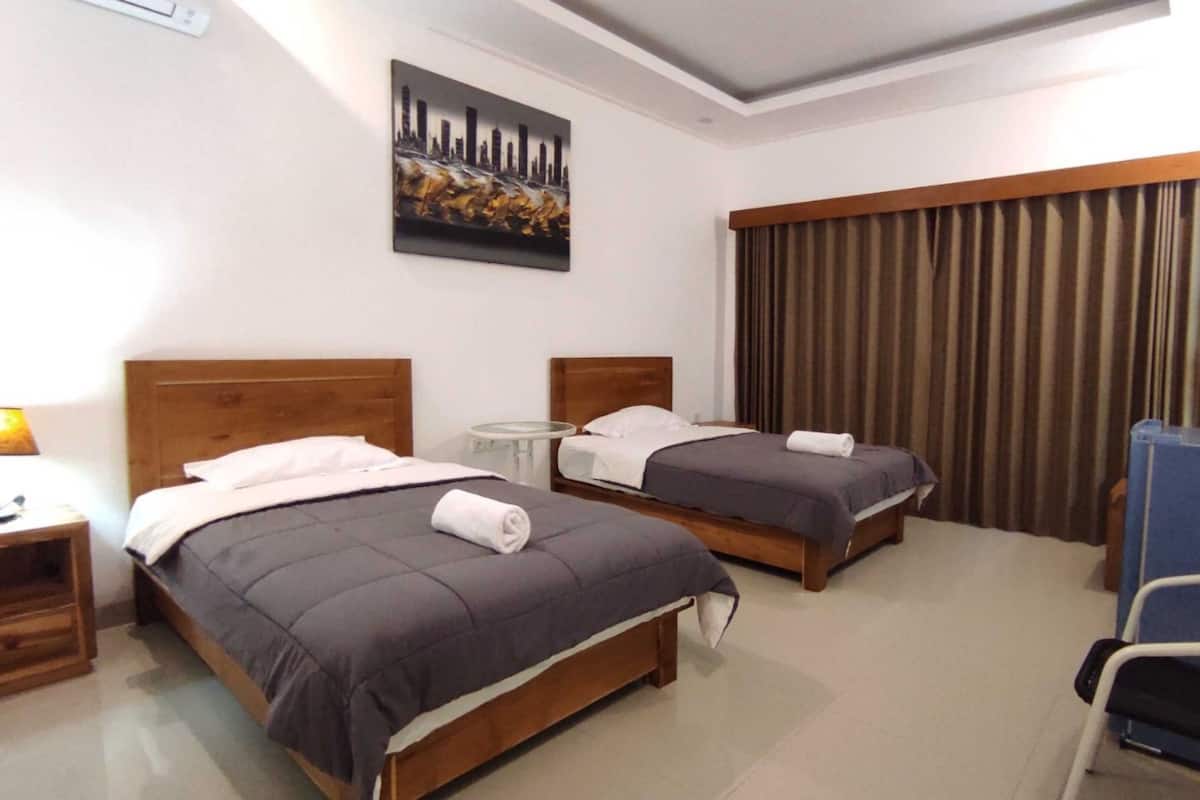 A hotel room with two beds, a desk, a chair, a TV, and a painting on the wall.