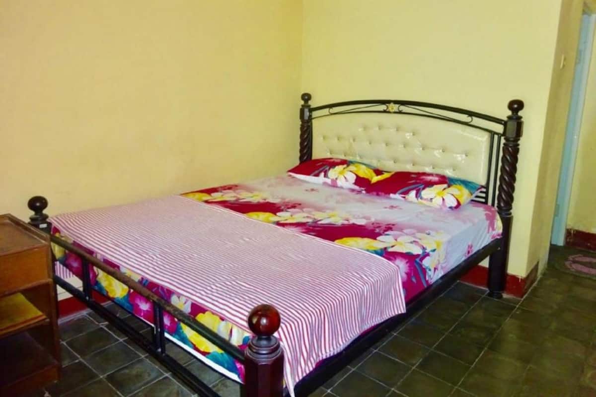 A single bed with a floral bedspread and a striped pillow, a wooden headboard, and a small bedside table.