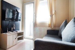 Ein modernes Wohnzimmer mit einem Flachbildfernseher an einer dunklen Wand, einem Holztisch mit Elektronik, einem grauen Sofa und einem großen Fenster mit Vorhängen.