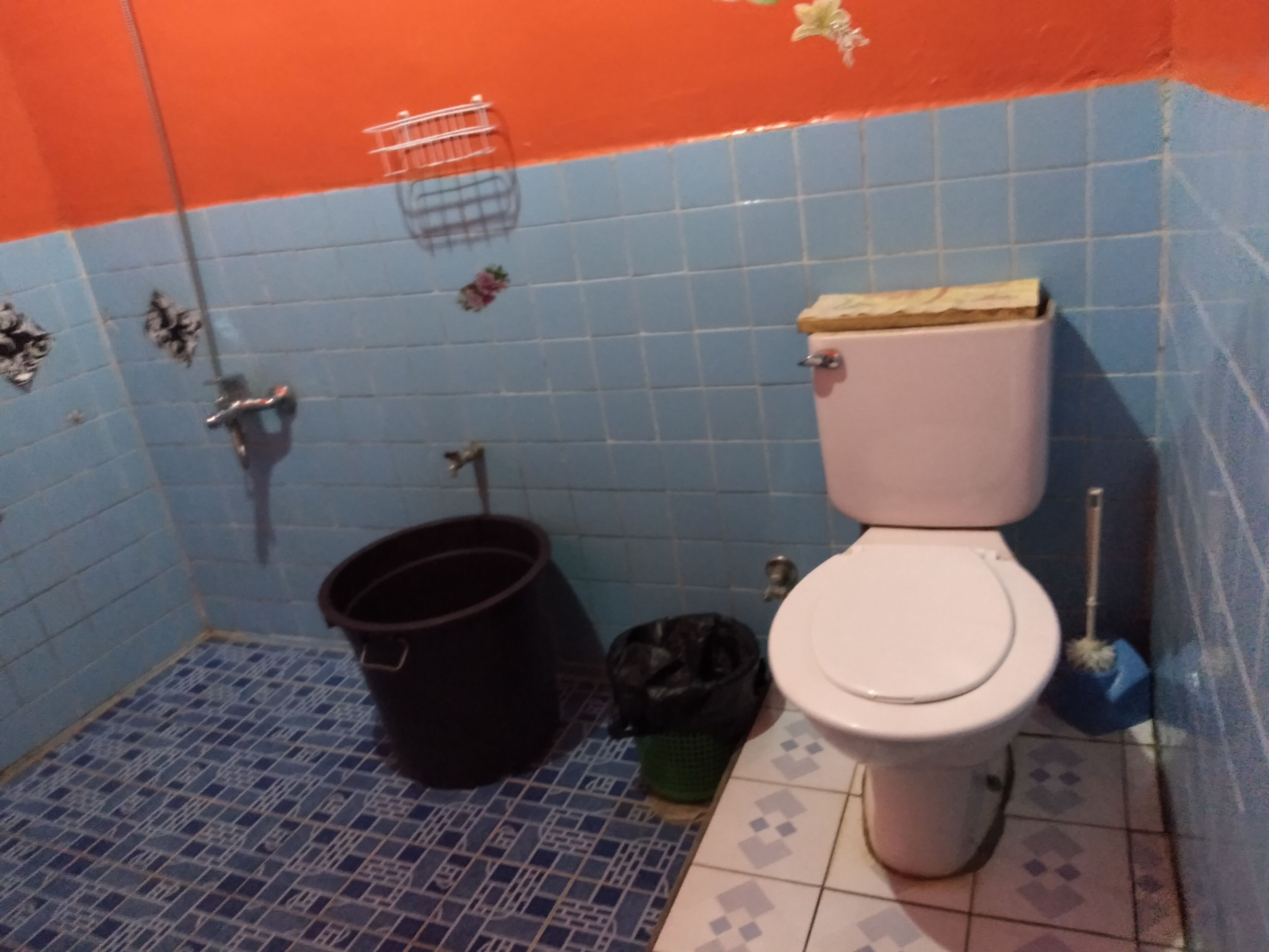 A small bathroom with a toilet, a bucket, and a broom.
