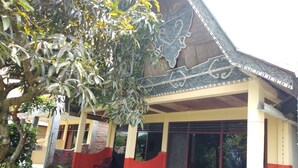 A covered outdoor seating area with chairs and a table, surrounded by a building with a decorative roof and a red and yellow color scheme. - Merlyn Guest House (Samosir)