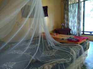 Una cama con mosquitero, una colcha estampada con motivos florales y una mesita con un jarrón de flores.