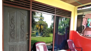 A room with a sliding glass door leading to a garden, two plastic chairs, and a small table. - Merlyn Guest House (Samosir)