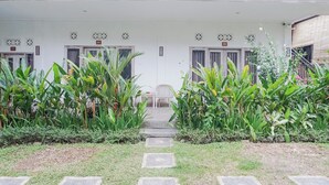 A building with numbered doors, a staircase leading to the entrance, and a garden with large plants. - Karan Homestay Canggu (Canggu)