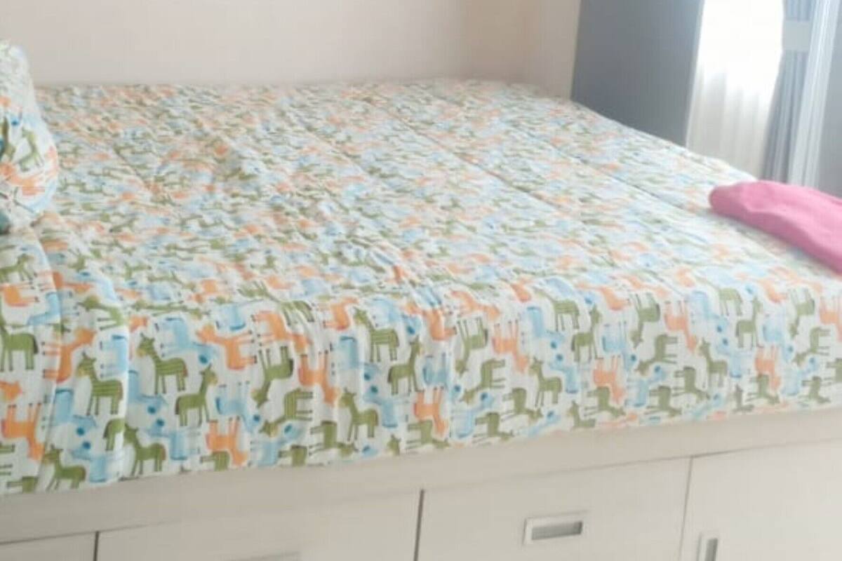 A bedroom with a bed, drawers, and a window with curtains.