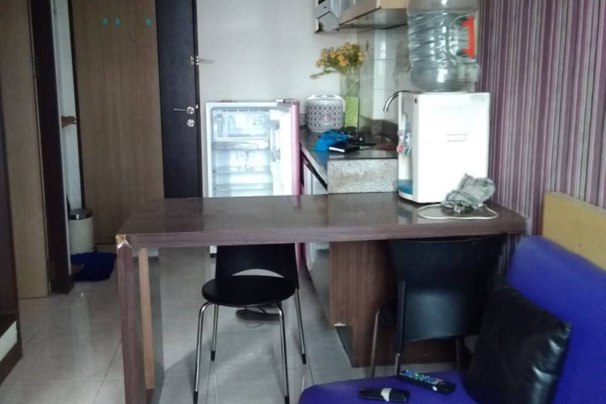 A compact living space with a kitchenette, a dining table, a blue sofa, and a water dispenser.