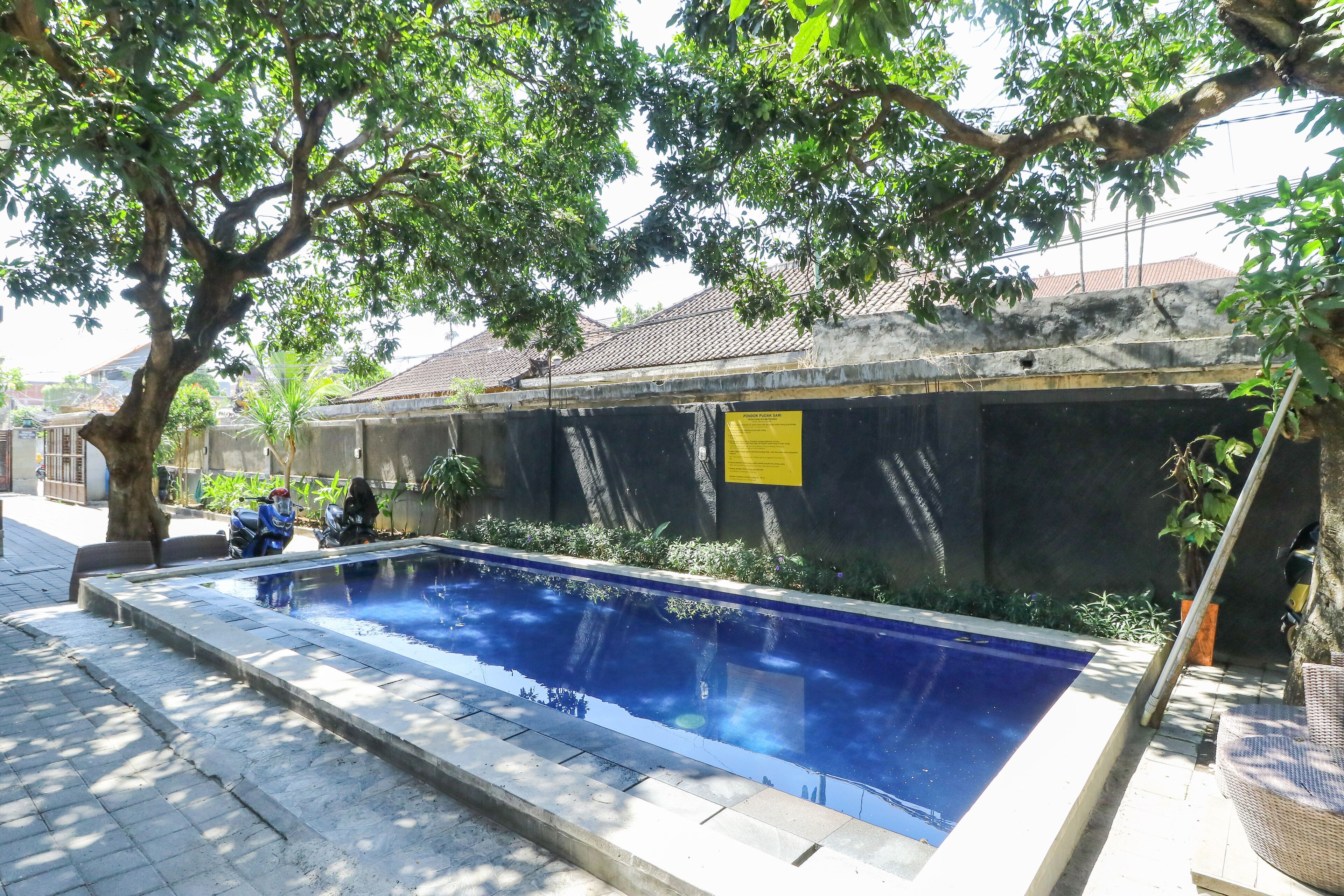 A swimming pool with a tiled edge, surrounded by a low brick wall, and shaded by trees.