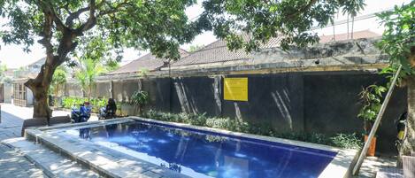 A swimming pool with a tiled edge, surrounded by a low brick wall, and shaded by trees.