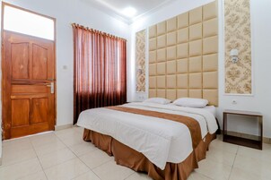 Un dormitorio con puerta de madera, una cama con cubrecama blanco y marrón, un cabecero capitonado y una mesita de noche pequeña.