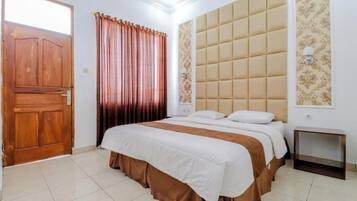 A bedroom with a wooden door, a bed with a white and brown bedspread, a headboard with a tufted design, and a small bedside table.