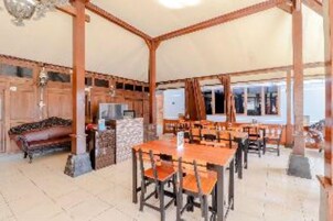 Un comedor amplio con mesas y sillas de madera, una chimenea de piedra y ventanas grandes.