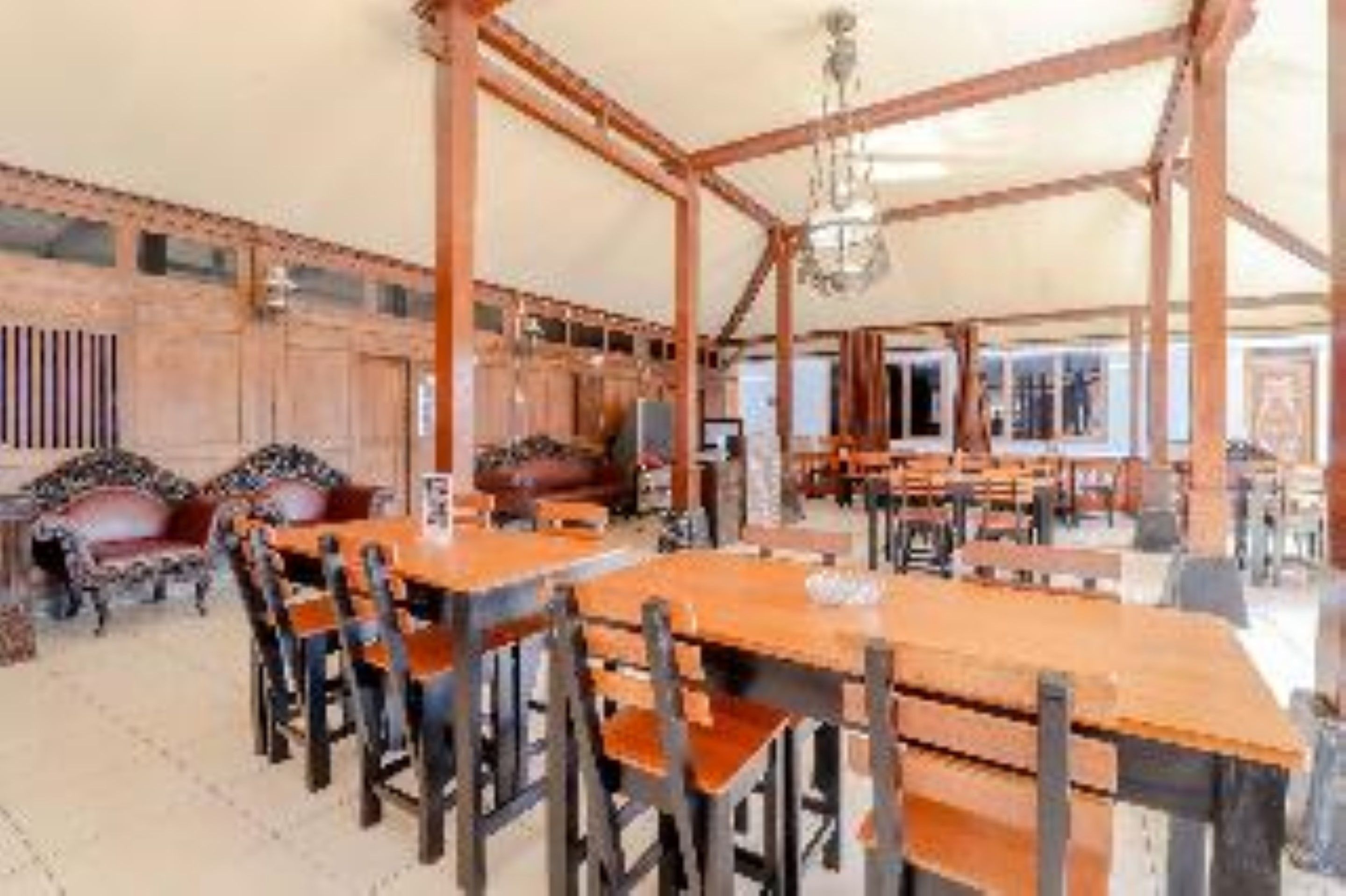 A spacious room with wooden tables and chairs, a chandelier, and a large window.