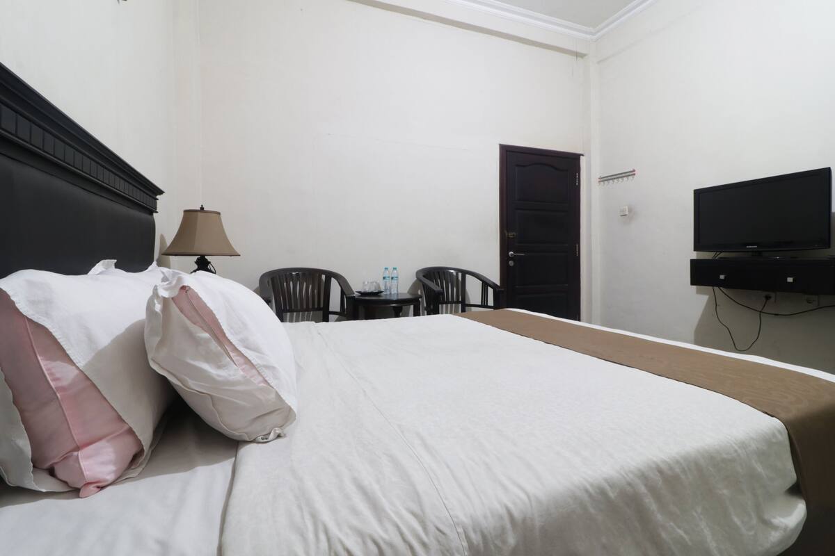 Una habitación de hotel con cama, televisión, escritorio con lámpara y una silla.