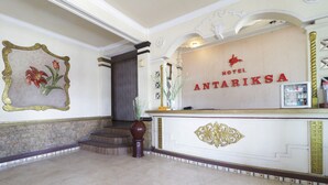 A reception area with a marble floor, a reception desk, a framed floral artwork, and a staircase leading to an upper level. - Hotel Antariksa (Surabaya)