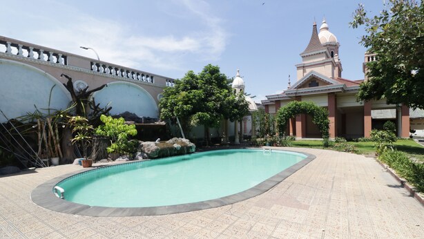 A swimming pool with a tiled walkway, surrounded by greenery and a building with a dome and tower. - Hotel Antariksa (Surabaya)