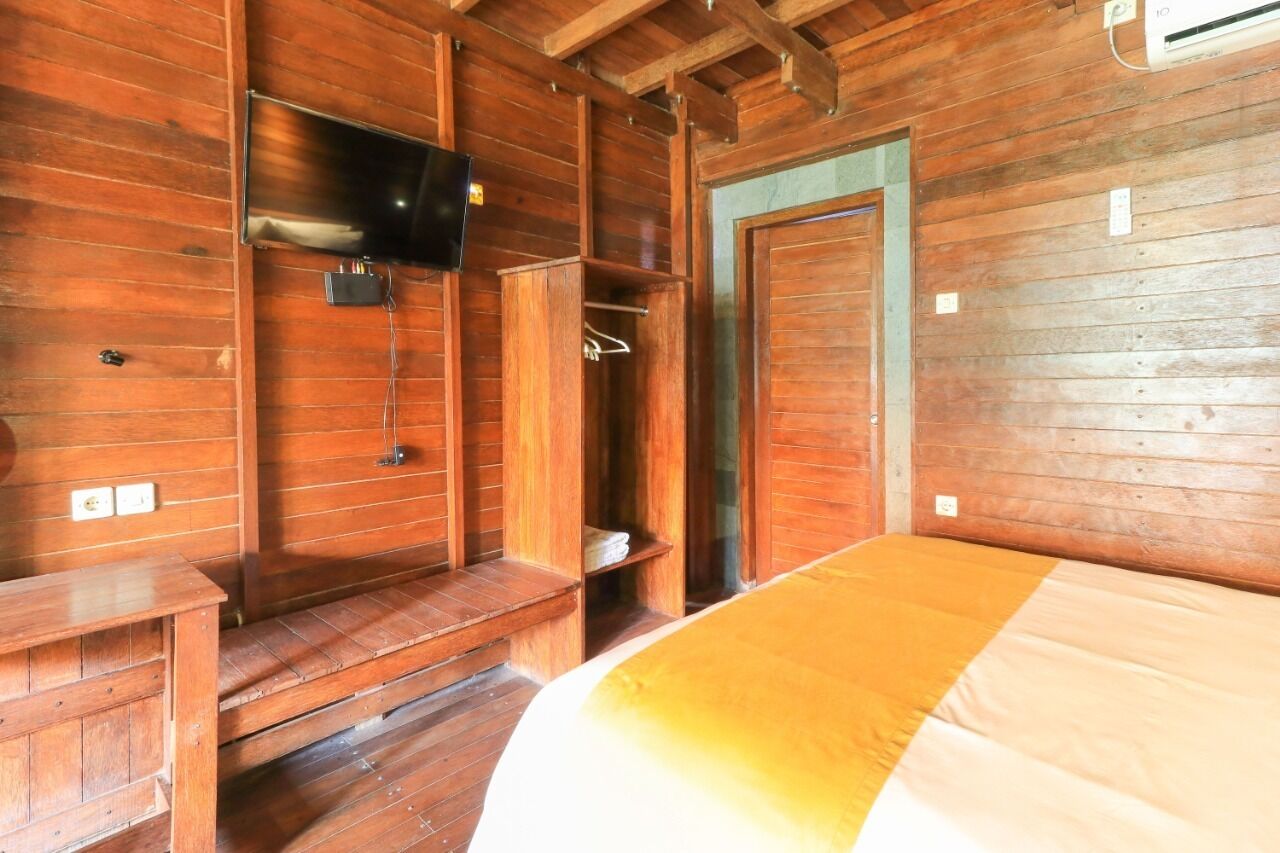 Een houten kamer met een bed, een aan de muur bevestigde televisie en een houten kledingkast.