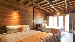A wooden cabin room with two beds, a wooden ceiling, and a window with curtains.