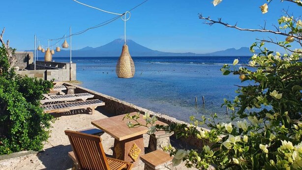 A seaside terrace with a view of the sea and a mountain in the distance.