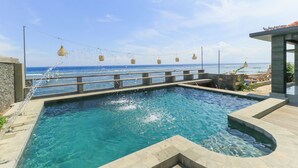 A swimming pool with a view of the ocean, surrounded by a stone deck and a wooden fence.