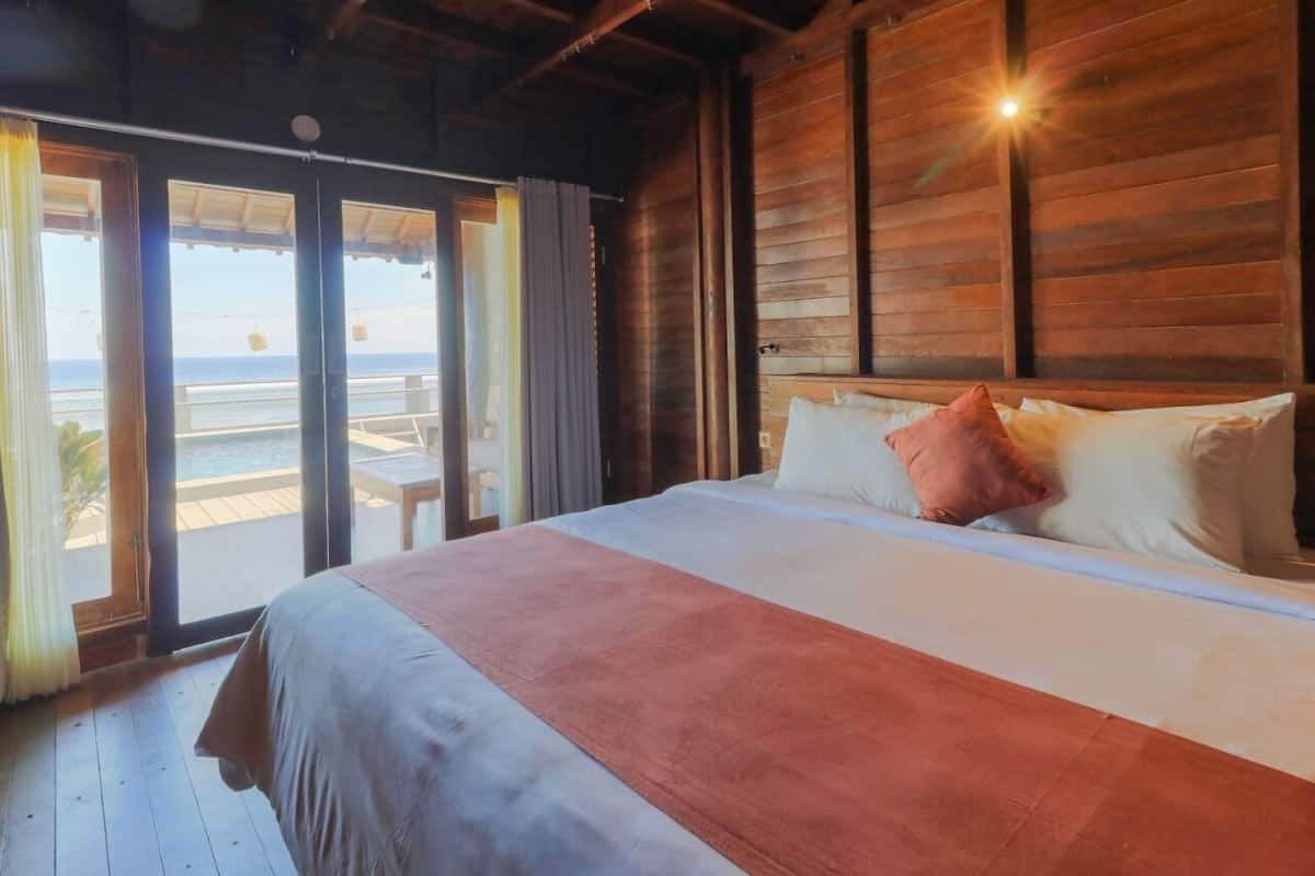 A wooden room with a bed, a view of the ocean, and a sliding door to the outside.