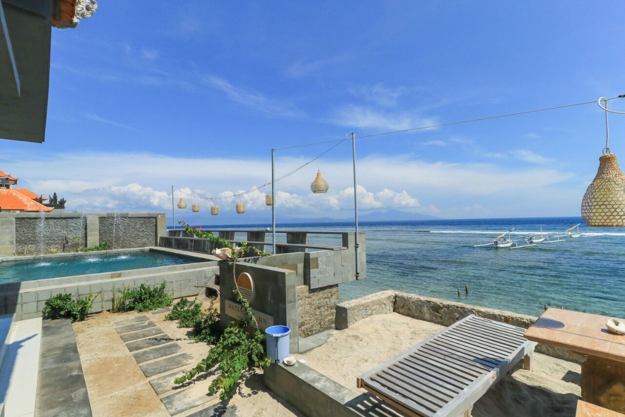 A rooftop pool area with a view of the sea, a pergola with hanging lights, and a lounge area with a table and chairs.
