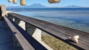 A wooden pier extending into a clear blue sea with a mountain in the background.
