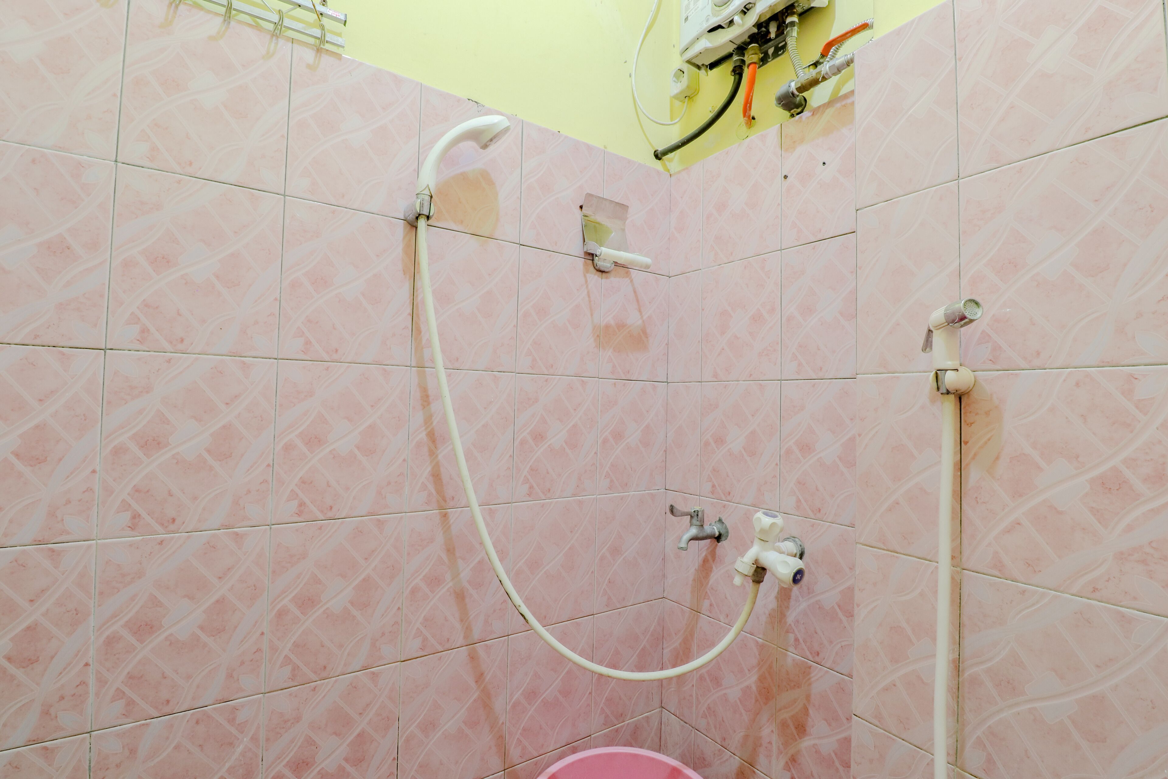 A bathroom with pink patterned tiles, a showerhead, and a visible pipe.